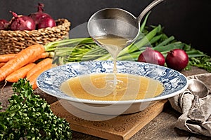 Pouring chicken bone broth from a ladle into a vintage plate