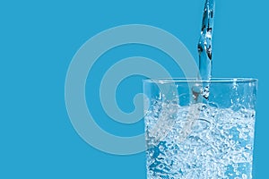 Pouring clean drinking water from blue plastic bottle into glass on blue background