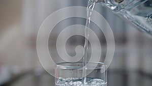 Pouring clean drinking water into glasses from a decanter, camera movement, close-up