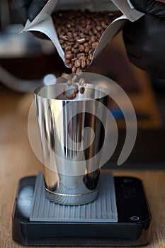 Pouring coffee beans from pack into metal glass on black acaia scales, closeup