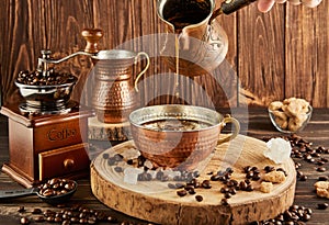 Pouring coffee from coffee maker into copper cup, an antique coffee grinder and copper milk jug on wooden background