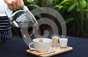 Pouring coffee into a cup on a wooden tray. placed on a table covered with a black tablecloth.