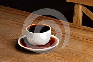 Pouring coffee into overflowed white porcelain mug with saucer. Cup with overflowing coffee. Full cup of coffee.