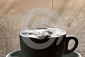 Pouring coffee into white porcelain mug with saucer from moka pot coffee maker. Mug on wooden table and stream of coffee.