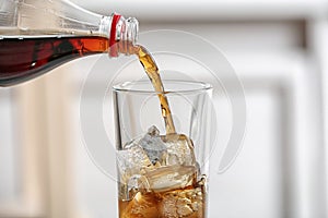 Pouring cola from bottle into glass on blurred background