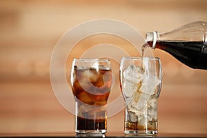 Pouring cola from bottle into glass with ice cubes on table