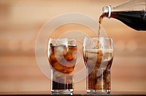 Pouring cola from bottle into glass with ice cubes on table