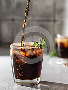Pouring Cola or cuba libre cocktail in glass with ice cubes and mint. Soft drink with splashing