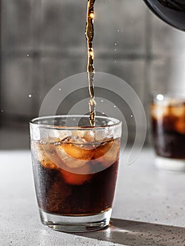 Pouring Cola or cuba libre cocktail in glass with ice cubes. Soft drink with splashing