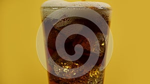 Pouring cola drink glass full of coke sparkling soda ice cubes yellow background