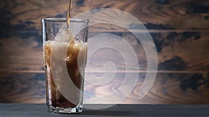 Pouring cola in glass with ice cubes