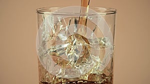 Pouring cola soft drink into a glass with ice cubes on brown background, slow motion shot on Red