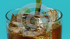 Pouring cola soft drink into a glass with ice cubes on cyan background, slow motion shot on Red