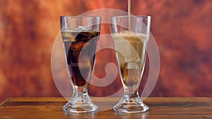 Pouring cola soft drink on ice in tall cafe glasses.