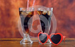 Pouring cola soft drink on ice in tall cafe glasses.