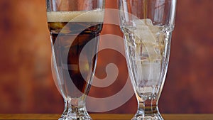 Pouring cola soft drink on ice in tall cafe glasses.