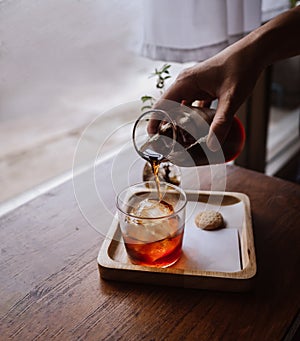 Pouring cold brew iced coffee in glass cup with ice cubes. Coffee In a glass bottle, Coffee drip, Hand holding a kettle drip