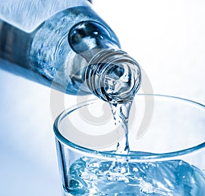 Pouring of cold clear drink water from bottle into glass, close