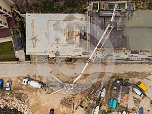 Pouring concrete cement on the roof of residential building under construction using a concrete pump truck machine with high boom