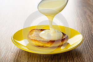 Pouring condensed milk from spoon on pancake in yellow saucer on table