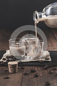 Pouring  Cream coffee liqueur in glasses with ice, surrounded by coffee beans on a dark wooden background