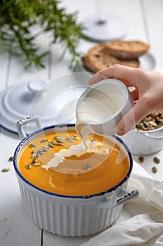 Pouring cream into yellow cream soup, the bowl on the white table