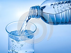 Pouring crystal water from bottle on glass on blue background