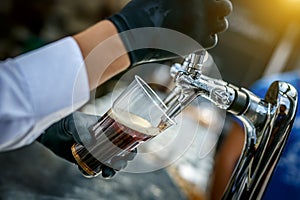 Pouring dark beer to plastic glass from beer tap.