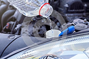 Pouring distilled water ecological alternative to washing fluid to washer tank in car, detail on clear plastic bottle