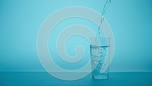 Pouring drink water to glass of water. Close up pouring fresh clean drinking water into glass, splashing in glass on light blue