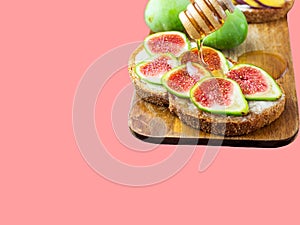 Pouring drizzling honey on sourdough toast with cream cheese topped with fresh ripe figs peaches