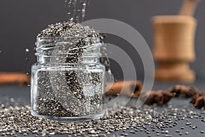 Pouring dry chia seeds in glass jar with unfocused objects on background. Copy space.