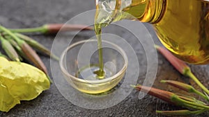 Pouring evening primrose oil from a bottle into a bowl, with fresh Oenothera biennis flowers, slow motion