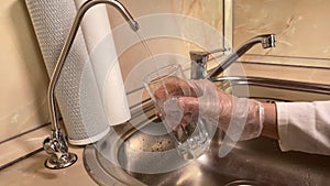 Pouring filtered water into glass from water filter. Closeup of sink and faucet. Drinkable water