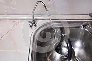 Pouring filtered water into kettle from water filter. Closeup of sink and faucet. Drinkable water photo