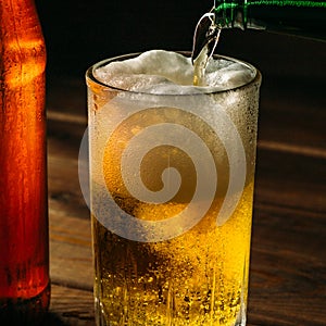 Pouring foaming beer into glass mug with drops near cold beer bootle, close up
