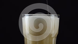 Pouring fresh and cold craft beer into a glass with white foam on top on black background. Flowing foamy wheat or lager beer on