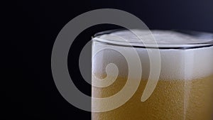 Pouring fresh and cold craft beer into a glass with white foam on top on black background. Flowing foamy wheat or lager beer on