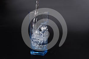 pouring fresh drink water to blue glass on black