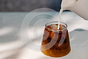 Pouring Fresh Milk into a Glass of Ice Coffee. Making Cold Drink in a hot Summer Day