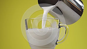 Pouring fresh milk in slow motion into a transparent glass cup from a metal pot.