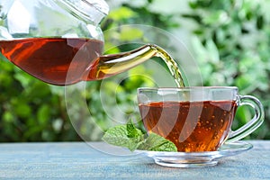 Pouring fresh mint tea into cup on blue wooden table, closeup