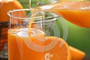 Pouring fresh orange juice in glass with sliced orange on nature background