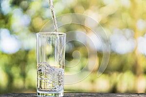 Pouring fresh water on drinking glass over nature sunlight morning background