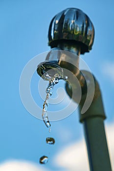 Pouring fresh water from the metal tap with blurred blue cloudy sky background