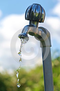 Pouring fresh water  from the metal tap with blurred nature and blue cloudy sky background