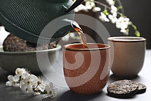 Pouring freshly brewed pu-erh tea into cup on grey table, closeup