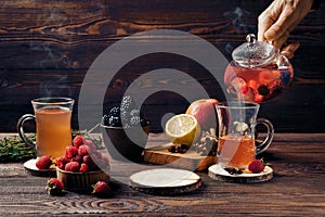 Pouring fruit tea with raspberries, bramble, apple and lemon in cup