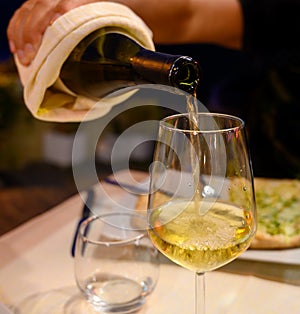 Pouring in glass  cold dry white wine in outdoor cafe at night in Italy