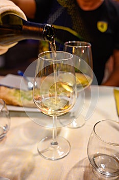 Pouring in glass  cold dry white wine in outdoor cafe at night in Italy